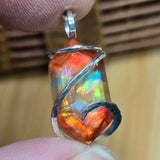 Multicolored Ammolite pendant with silver wire wrapping held between fingers against a wooden background