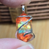 Multicolored Ammolite pendant with silver wire wrapping held between fingers against a wooden background