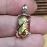 Ammolite pendant held between fingers with a blurred background