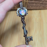 Decorative key-shaped object with a colorful gemstone held by a hand against a wooden background