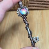 Decorative key with a colorful gemstone held by a hand against a wooden background