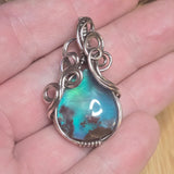 Aurora Opal Moss Agate Triplet stone pendant with silver wire wrapping held in a hand.