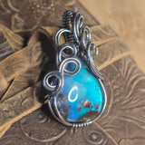 Silver wire-wrapped pendant with a blue and purple stone on a textured surface
