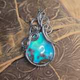 Aurora Opal stone pendant with silver wire wrapping on a textured brown surface