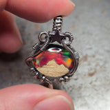 Close-up of a hand holding a colorful pendant with intricate metalwork.