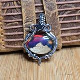 Silver pendant with a colorful mountain design on a wooden surface