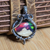 Silver pendant with a colorful mountain design on a wooden surface