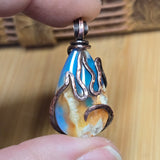 Close-up of a flame-shaped pendant held between fingers with a wooden background