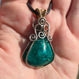 Teal stone pendant with silver and gold accents held in a hand.