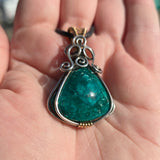 Chrysocolla pendant with silver and gold accents held in a hand.