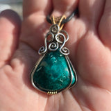 Chrysocolla pendant with silver and gold accents held in a hand