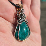 Teal stone pendant with silver and gold accents held in a hand.