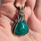 Chrysocolla pendant with silver and gold accents held in a hand