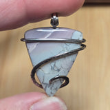 Blue and purple Jasper pendant held between fingers on natural backgroundBlue and purple Jasper pendant held between fingers on natural background