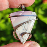 Blue and purple Jasper pendant held between fingers on blurred green background