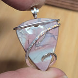 Pink Blue Purple stone pendant with silver wire wrapping held between fingers against a beige background.