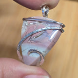 Silver-wrapped stone pendant held between fingers against a blurred background