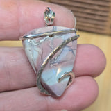 Pendant with a stone and silver wire wrapping held between fingers