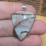Silver pendant with a pink blue purple stone held between fingers