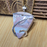 Silver-wrapped pink blue purple stone pendant on a wooden surface