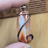 Hand holding a decorative pendant with a wire wrap design against a wooden background