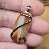 Agate pendant with copper wire wrap held in a hand against a wooden background