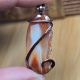 Agate pendant with copper wire wrapping held by a hand against a wooden background