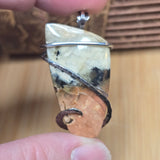Close-up of a stone pendant with wire wrapping held between fingers against a wooden background