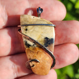 Hand holding a stone pendant with a blurred green background