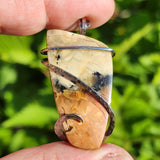 Hand holding a unique stone pendant with a natural green background