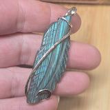Feather-shaped pendant held between fingers with a wooden background