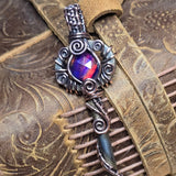 Decorative key with Aurora opal gem on a leather-bound book with floral patterns.