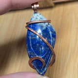 Blue stone pendant with copper wire wrapping held by a hand on a wooden surface