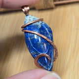 Blue stone pendant with copper wire wrapping held by a hand on a wooden surface