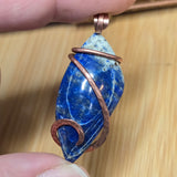 Blue stone pendant with copper wire wrapping held by a hand on a wooden surface
