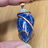 Blue stone pendant with copper wire wrapping held by a hand on a wooden surface