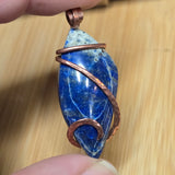 Blue stone pendant with copper wire wrapping held by a hand on a wooden surface