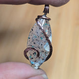 Close-up of a speckled pendant held between fingers against a blurred background
