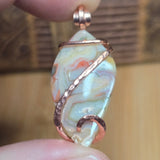 Jewelry pendant with crazy lace stone and copper wire wrapping held between fingers.