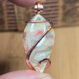 Marbled stone pendant with copper wire wrapping held between fingers against a blurred background
