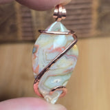 Marble-like pendant with copper wire wrapping held between fingers against a blurred background