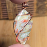 Marbled stone pendant with copper wire wrap held in hand against a blurred background