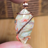 Marbled stone pendant with copper wire wrapping held by a hand against a blurred background