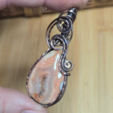 Copper-wire wrapped pendant with a natural stone on a wooden surface