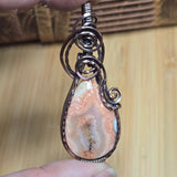 Teardrop-shaped pendant with wire wrapping on a wooden surface