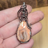 Jewelry pendant with stone and wirework held in a hand against a blurred background