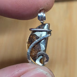 Silver pendant with a textured design held between fingers against a blurred background