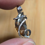 Silver pendant with a textured design held between fingers against a blurred background