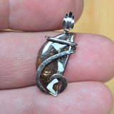 Silver pendant with a brown stone held between fingers
