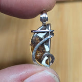 Silver pendant with a brown stone held between fingers against a blurred background